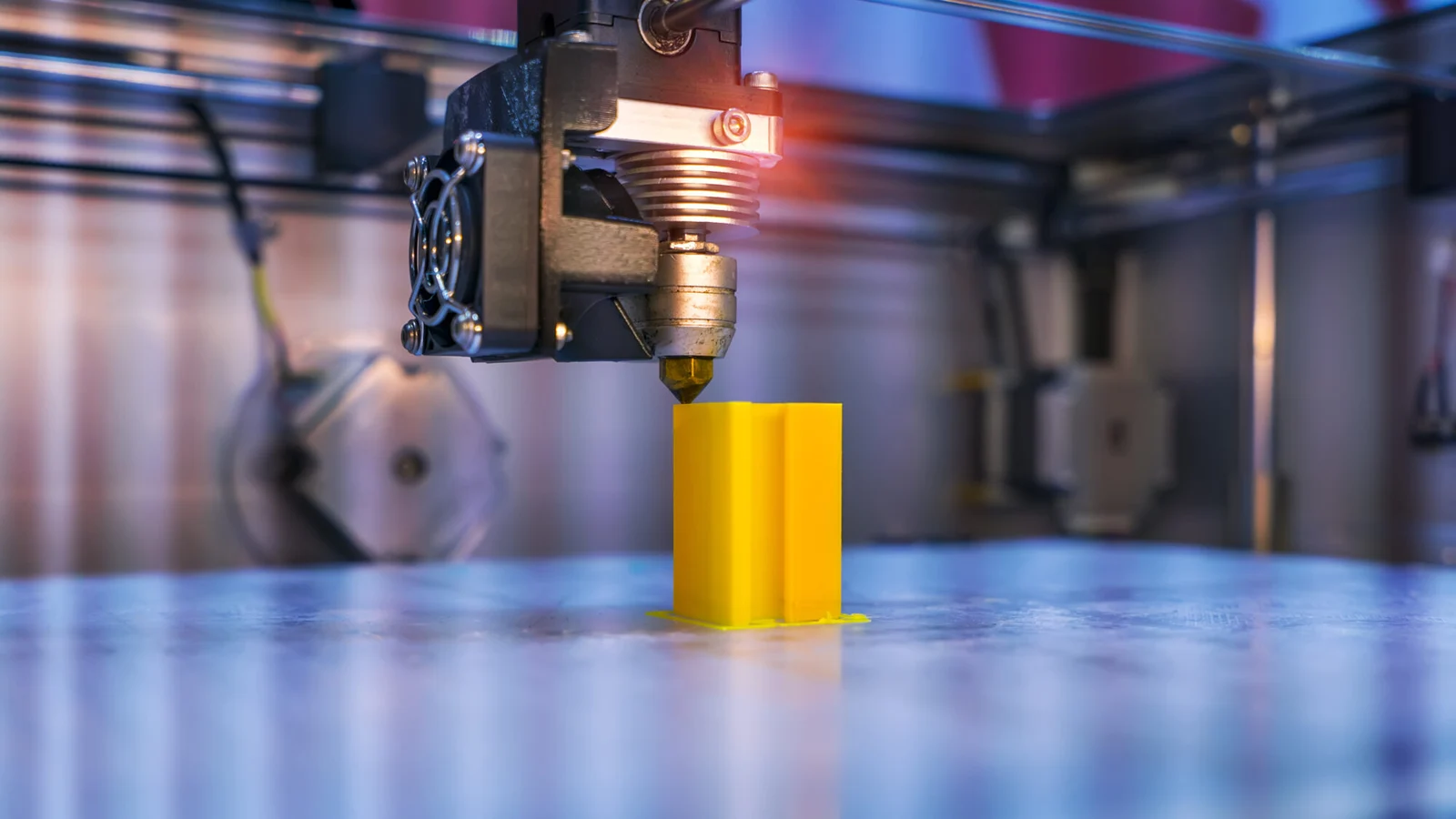 Close view of a 3D printer depositing a yellow component; illustrative manufacturing image